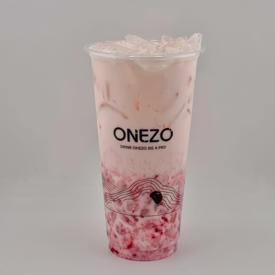 Pink berry milk tea with ice in a clear Onezo cup, featuring fruit pieces and tapioca pearls.
